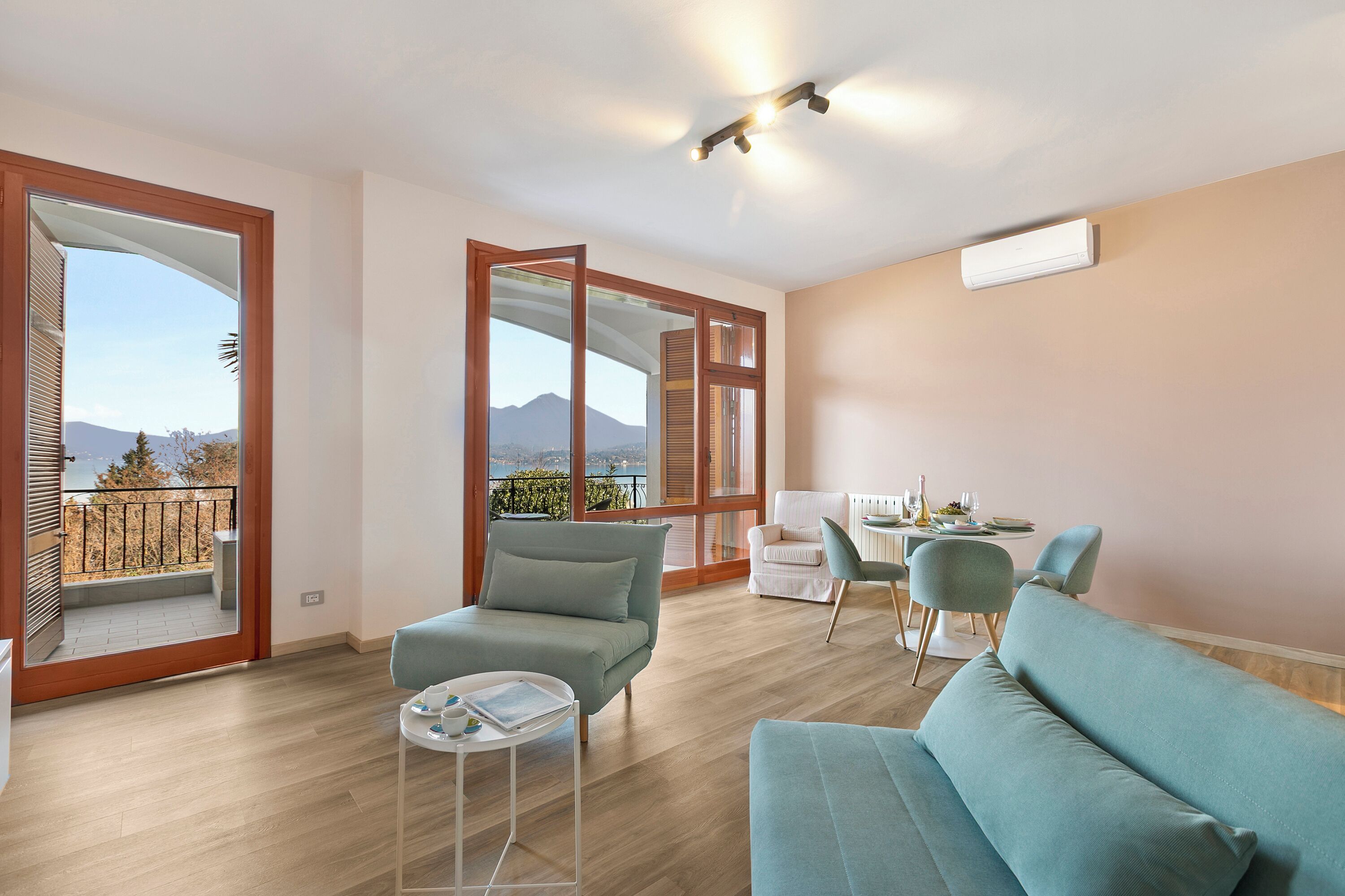 A modern living room with a sofa, chairs, a dining table, and large windows offering a view of mountains.