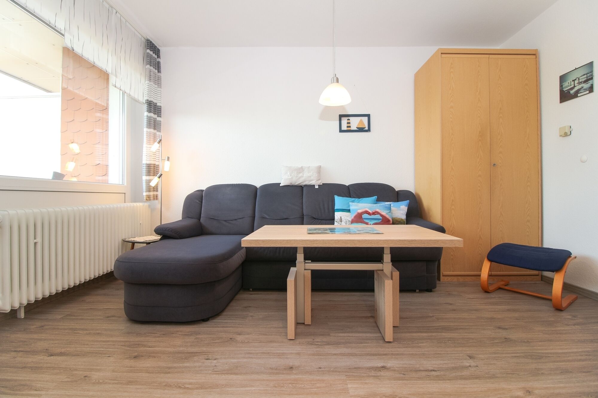 Een knus vertrek met een bank, een kleine tafel, een bankje en een radiator.