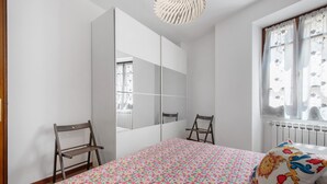 Ein Schlafzimmer mit Bett, Stuhl, Kleiderschrank und einem Fenster mit Vorhängen.