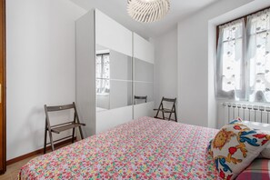 A bedroom with a bed, a chair, a wardrobe, and a window with curtains.