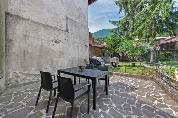 An outdoor patio with stone flooring, a table with chairs, and a grill area.