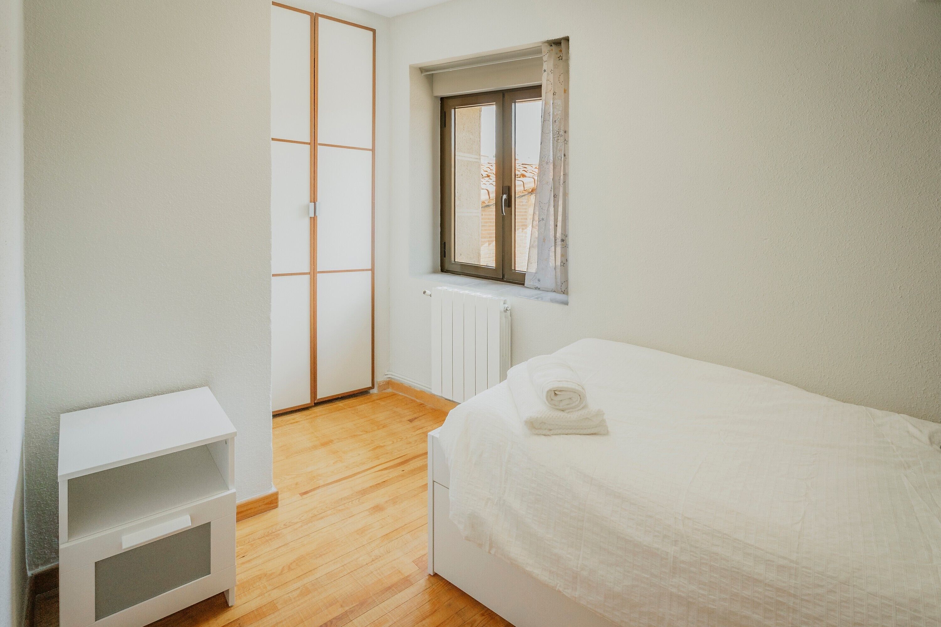 Une chambre à coucher avec un lit, une table de chevet, une fenêtre et un radiateur.
