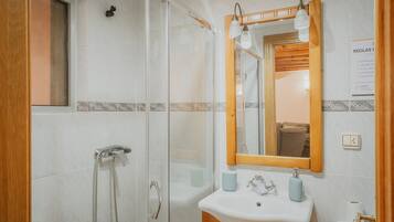 Een badkamer met een douchecabine van glas, een houten wastafelmeubel met een spiegel en een witte wastafel.