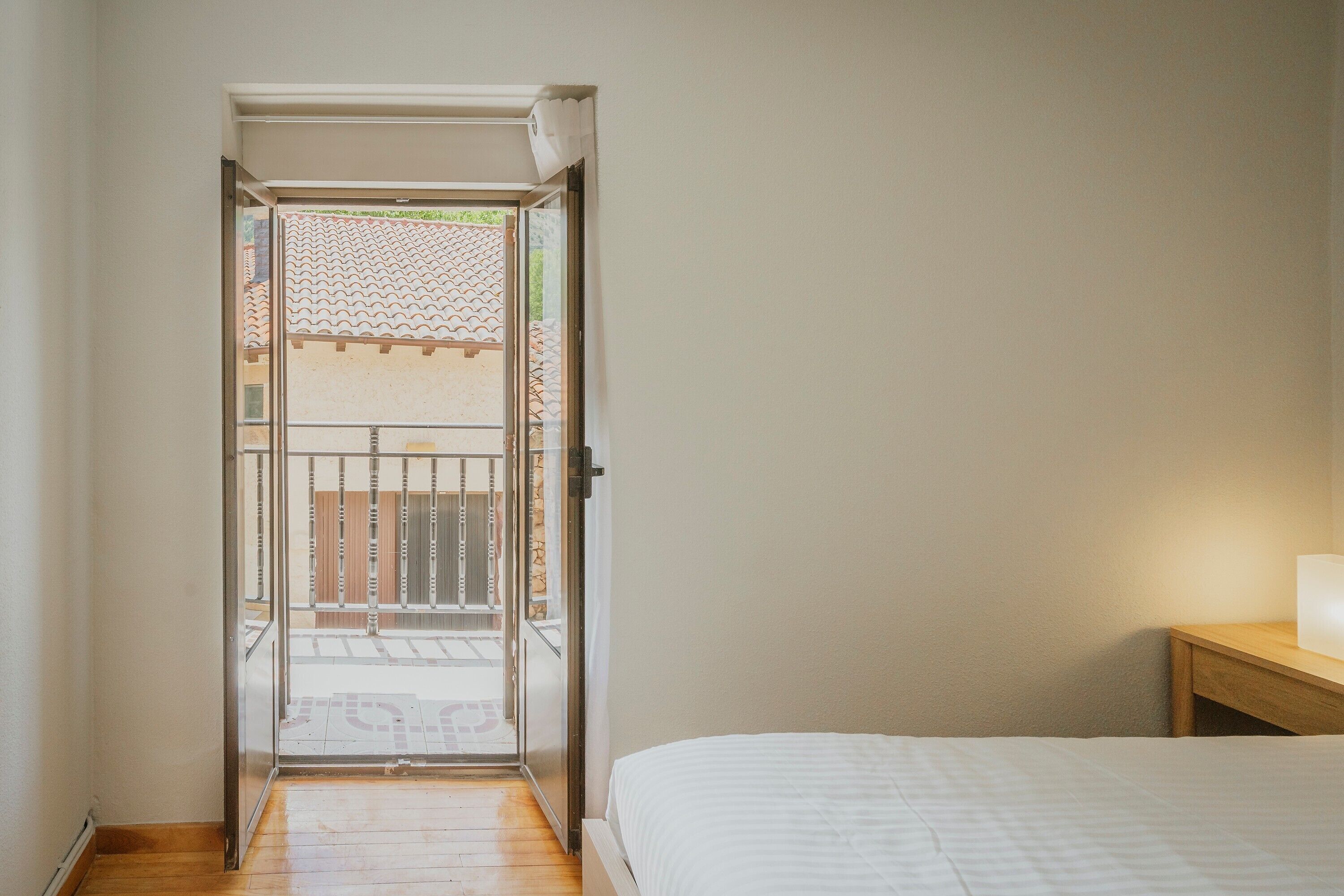 A bedroom with a bed, a nightstand, and a view through an open door to an outdoor balcony.