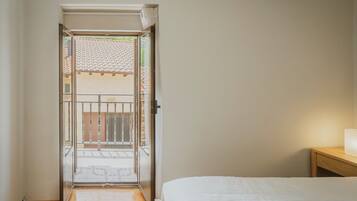 A bedroom with a bed, a nightstand, and a view through an open door to an outdoor balcony.