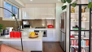 A modern kitchen with white cabinets, a central island, and a built-in bookshelf. - Soft Modern Glamour in the Heart of Camberwell (Camberwell)