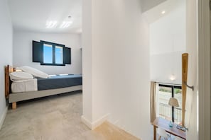 A bedroom with a bed, a window, a table, and a view of the outside.