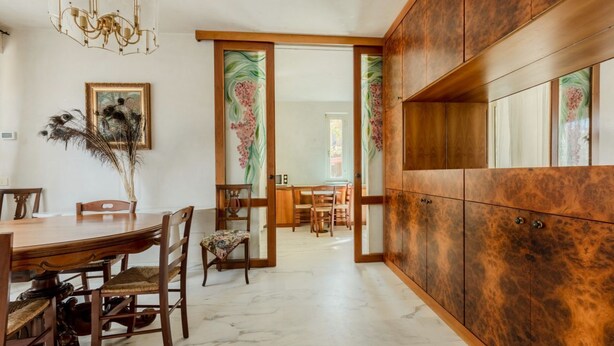 A dining area with a wooden table and chairs, a chandelier, and a cabinet with a textured surface.