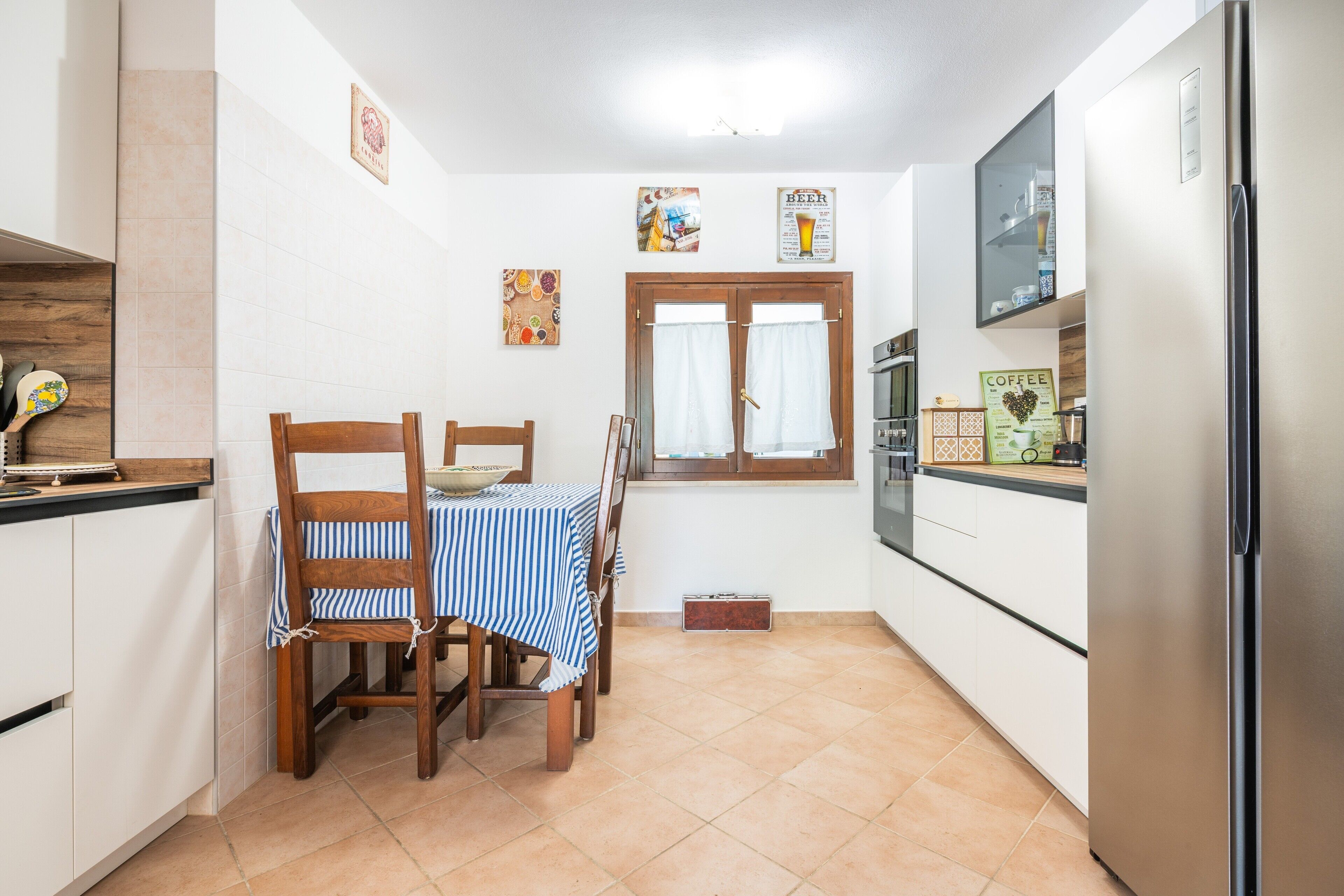 Een keuken met een eettafel, stoelen, een koelkast en een raam met gordijnen.