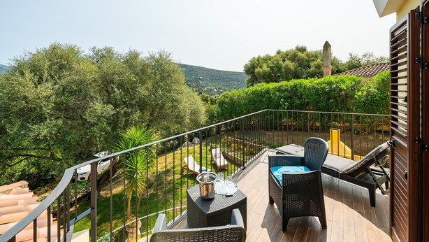 A balcony with wicker furniture, a table, and a view of a lush garden and distant hills. - Holiday Home 'L'ulivo' a few steps from the sea with Garden View, Wi-Fi and Air Conditioning (Torre Delle Stelle)