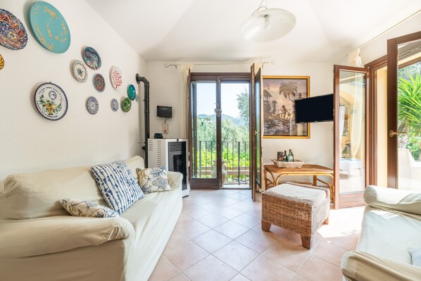 A living room with a sofa, a television, a dining table, and a balcony with a view.