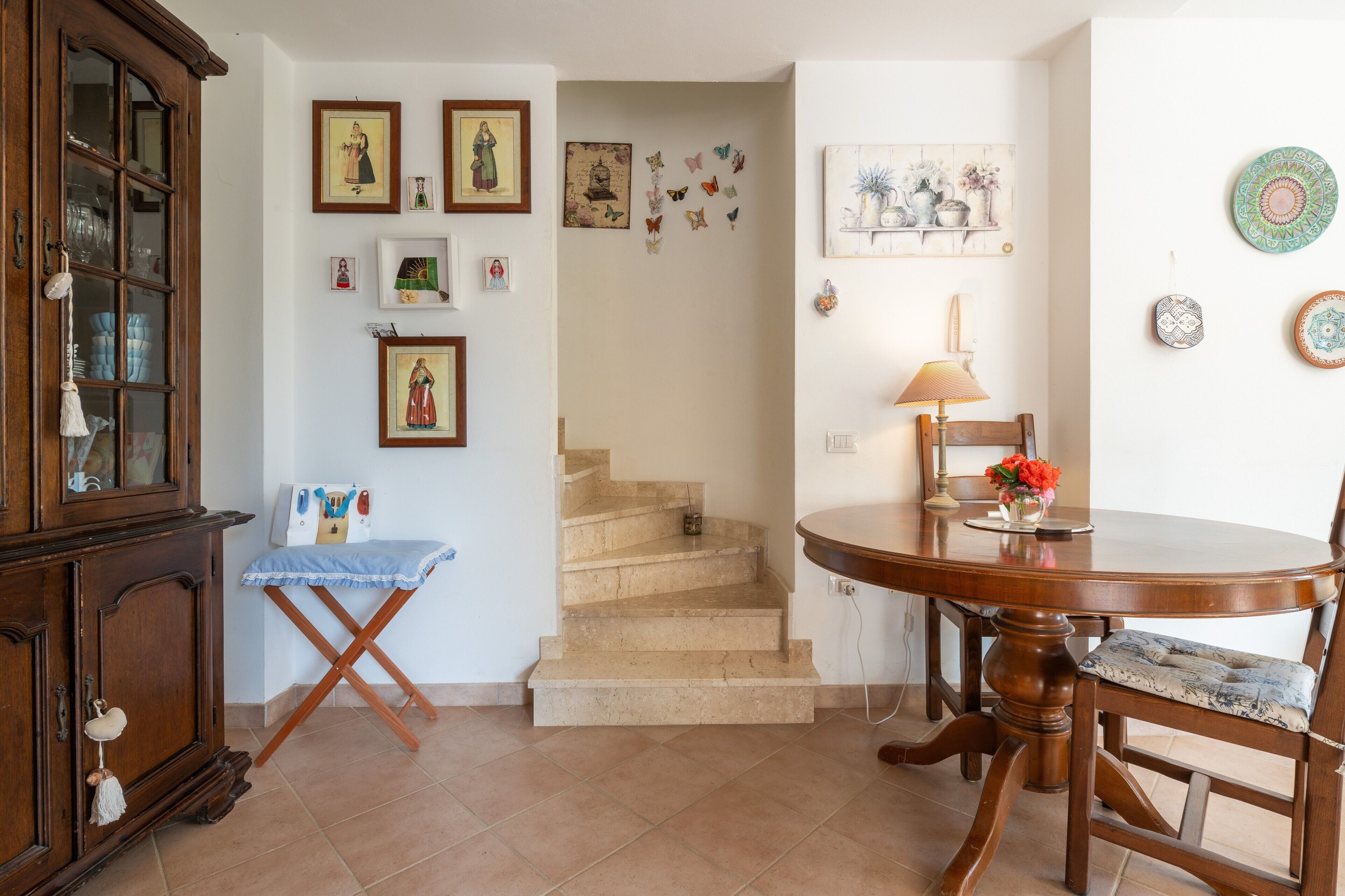Ein Zimmer mit einem Holzkabinett, einem Esstisch mit Stühlen, einer Treppe und verschiedenen Wanddekorationen.