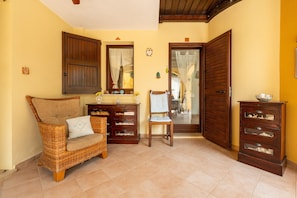 A room with a wicker sofa, a wooden chair, a cabinet with drawers, and a door with a wooden shutter.