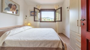 A bedroom with a bed, a window with a view, a bedside lamp, and a wardrobe. - Holiday Home 'L'ulivo' a few steps from the sea with Garden View, Wi-Fi and Air Conditioning (Torre Delle Stelle)