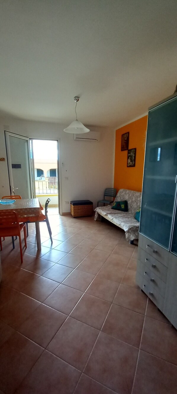 A room with a dining table, chairs, a sofa, a cabinet, and a door leading to an outdoor area. - Holiday Home 'Nicola' with Private Terrace and Air Conditioning (Salve)