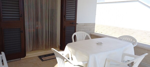 Un balcon avec une table et des chaises, une porte en bois et une vue sur la plage.