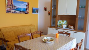 A dining area with a table set for two, a yellow sofa, wooden chairs, a cabinet with glass doors, and a wall with a painting. - Holiday Home 'Villetta Lucy' with Sea View, Private Terrace and Air Conditioning (Salve)