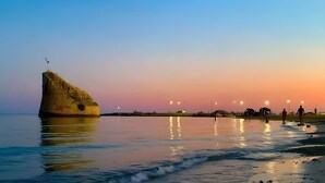A beach with a large rock formation, calm water, and distant lights. - Holiday Home 'Villetta Lucy' with Sea View, Private Terrace and Air Conditioning (Salve)