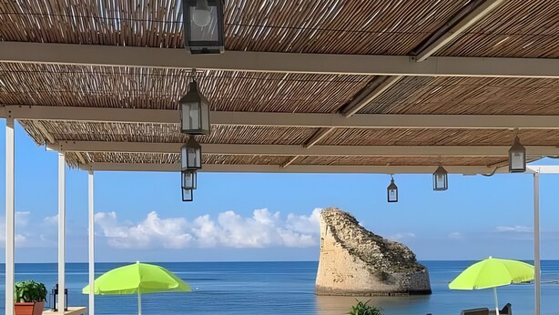 An outdoor seating area with tables and chairs, a pool, and a view of the sea and a rocky outcrop. - Holiday Home 'Villetta Lucy' with Sea View, Private Terrace and Air Conditioning (Salve)