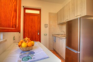 A kitchen with a wooden door, a stainless steel refrigerator, and a table with a fruit bowl.