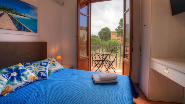 A bedroom with a bed, a painting, an open door to a balcony, and a TV on the wall.