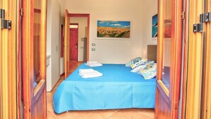 A bedroom with a blue bedspread, white towels, and a painting of a field.