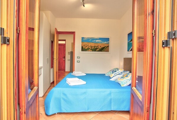 A bedroom with a blue bedspread, white towels, and a painting of a field.