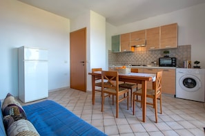 A compact kitchen with a washing machine, a dining table with chairs, and a refrigerator.