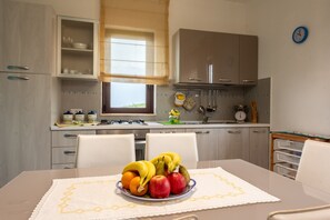 A kitchen with a dining table set for two, a window with blinds, and a clock on the wall.