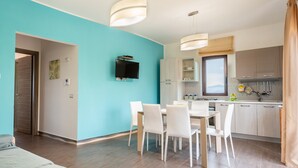 Une cuisine moderne avec des meubles blancs, un coin repas comprenant une table et des chaises, et un téléviseur fixé au mur.