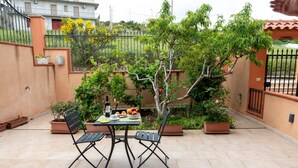 Une terrasse extérieure avec une table et des chaises, entourée de plantes en pot et d’une clôture.