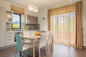 A modern kitchen with a dining area, including a table with chairs, a stove, and a window with curtains.