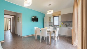 Une cuisine moderne dotée d’un téléviseur à écran plat, d’un coin repas avec des chaises blanches et d’un mur d’accent de couleur turquoise.