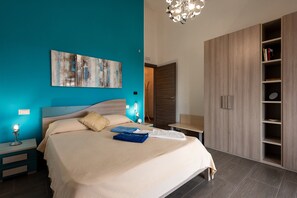 Une chambre à coucher comprenant un lit, une table de chevet, une lampe fixée au mur, un tableau, une armoire et un luminaire au plafond.