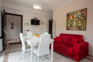 A dining area with a white table and chairs, a red sofa, and a colorful abstract painting on the wall.