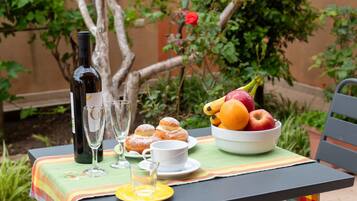 A table with a bottle of wine, glasses, a bowl of fruit, and pastries.