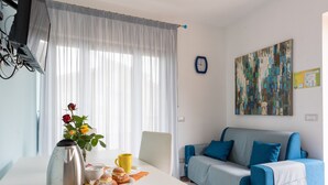 Ein Zimmer mit einem weißen Tisch, einem blauen Sofa, einem Bild an der Wand und einer Uhr.