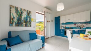Ein modernes Wohnzimmer mit einer Couch und einem Esstisch, eine Küche mit blauen Schränken und ein großes abstraktes Gemälde an der Wand.