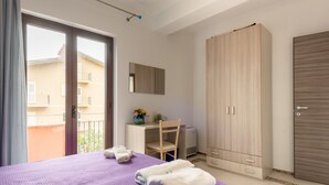 Ein Schlafzimmer mit Bett, Schreibtisch, Stuhl, Kleiderschrank und Balkonblick.