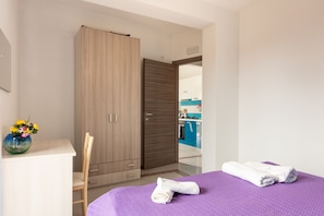 A bedroom with a bed, a wardrobe, a desk with a vase of flowers, and a view into the kitchen. - Apartment 'Luna Calante' with Sea View, Wi-Fi and Air Conditioning (Tusa)