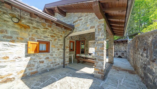 A stone building with a wooden porch, a bench, and a door leading to an interior space. - Holiday Home 'La Rosa Bianca' with Mountain View, Private Terrace and Wi-Fi (Morbegno)