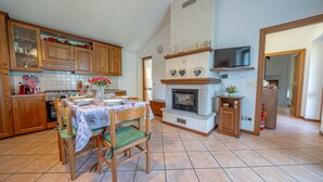 A kitchen with wooden cabinets, a dining table with chairs, a fireplace, and a television mounted above it. - Holiday Home 'La Rosa Bianca' with Mountain View, Private Terrace and Wi-Fi (Morbegno)