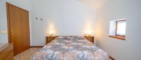 Un dormitorio con cama, cómoda de madera, lámparas de noche y ventana.