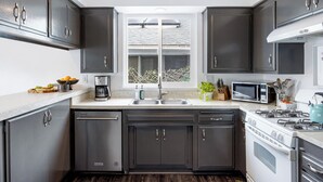 Une cuisine moderne avec des meubles de couleur sombre, un évier en acier inoxydable, un four à micro-ondes encastré et une cuisinière à gaz.