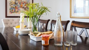 Une table à manger avec une assiette blanche, un bocal en verre, une bouteille et un panier de pain.