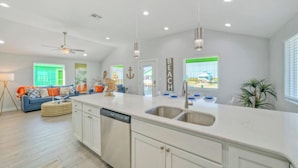 A modern kitchen with white cabinetry, a large island with a sink, and a ceiling fan. - Sleeps 21, 2 Homes | Private Pool, Covered Patio Lounge, Bar, TV, & Games (Port Aransas)