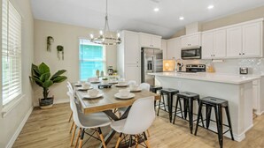 A modern kitchen with white cabinets, a wooden dining table, and black bar stools. - Sleeps 21, 2 Homes | Private Pool, Covered Patio Lounge, Bar, TV, & Games (Port Aransas)