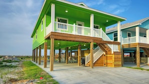 A two-story house with a green exterior and a wooden deck. - Sleeps 21, 2 Homes | Private Pool, Covered Patio Lounge, Bar, TV, & Games (Port Aransas)