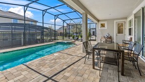 A covered outdoor pool area with a glass enclosure, a table with chairs, and a view of neighboring houses. - Pool, Hot Tub+Game Rm, Mins to Disney & Universal | Sunshine Ridge by AvantStay (Kissimmee)