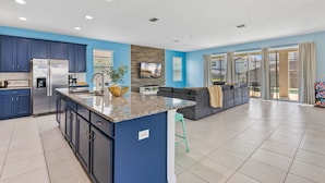 A modern kitchen with blue cabinets, a granite countertop, and a built-in island. - Pool, Hot Tub+Game Rm, Mins to Disney & Universal | Sunshine Ridge by AvantStay (Kissimmee)